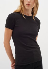 Svart kortärmad ribbad t-shirt gjord av mjukt tyg, med rund hals och en figurnära silhuett, bärs med mörka byxor.
