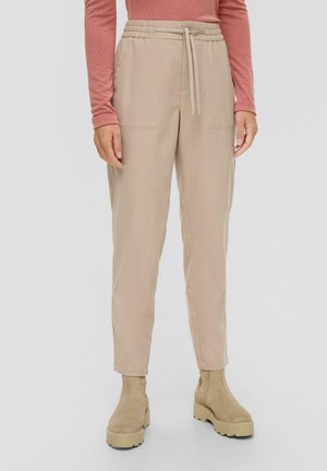 Beige tapse broeken met een elastische tailleband en strikkoord. Zachte stof met zijzakken. G gedragen met beige enkellaarsjes.