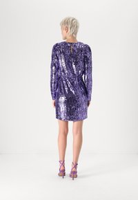 Vestido roxo com lantejoulas, mangas longas, detalhe nas costas com buraco em forma de chave e um corte justo. Combinado com sapatos de salto roxos com tiras.