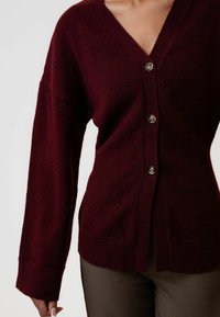 Bordo kardigan s V-izrezom, pet dugmadi naprijed, rebrasti manžeti i teksturiranim pletenim uzorkom, uparen s smeškim hlačama.