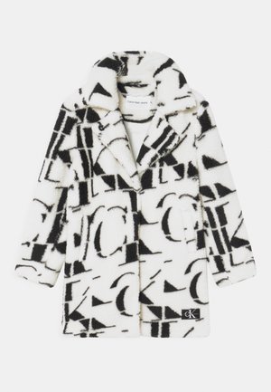 Valkoinen tekoturkistakki mustalla abstraktilla Calvin Kleinin logokuvioinnilla, leveällä kauluksella, pitkillä hihoilla ja etutaskuilla.