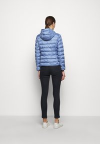 Jasnoniebieska puchowa kurtka z kapturem, z poziomymi pikowanymi sekcjami. Noszona na ciemnych legginsach i białych trampkach.