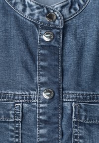 Close-up of blue denim fabric with three metal snap buttons labeled "BY STREET ONE DENIM" and visible stitching details.
