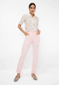 Bloemmotief polo shirt met korte mouwen en een kraag, gecombineerd met lichtroze rechte broek. Het model staat met de handen in de zakken.