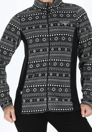 Zwart-witte gebreide trui met rits, met sneeuwvlok- en geometrische patronen, gedragen door een persoon met handen langs het lichaam.