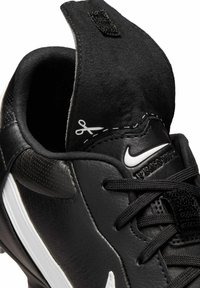 Fekete bőr focicipő lekerekített orrával, textúrázott felsőrésszel, fehér Nike logóval, és a hátán található tépőzárral a biztos illeszkedés érdekében.