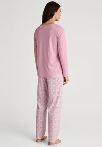 Lichtroze langarmtop gecombineerd met gestreepte broek met een bloemenpatroon in roze en wit. Zachte, ademende stof.