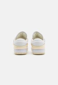 Sneakers bianchi in pelle con un colletto imbottito, caratterizzati da un morbido accento giallo, suola testurizzata e linee fluide. Vista posteriore che mette in evidenza gli elementi di design.