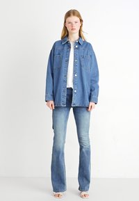 Keskmise sinise värviga denim-jakk, pikkade varrukatega, nööbid, kaks rinnataskut ja lõdva lõikega, koos helesiniste laiadest püksidest.