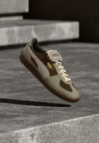 Sneaker z górną częścią wykonaną z brązowej i beżowej skóry, z wyściełanym kołnierzem, białymi sznurówkami i gumową podeszwą; logo Puma po bokach i na języku.