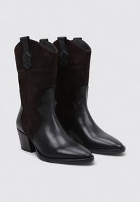 Botas de tobillo de estilo occidental en cuero negro y ante marrón oscuro, con punta afilada, tacón apilado, costuras decorativas y bucles para tirar.