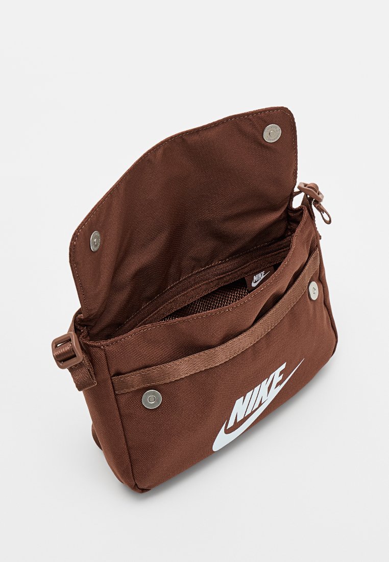 Bolso bandolera de tela marrón con correa ajustable, cierre magnético, bolsillo externo y logo blanco. El interior incluye un compartimento con cremallera.