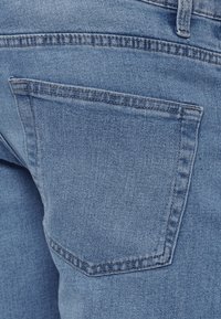 Ανοιχτό μπλε τζιν παντελόνι με πίσω τσέπη σε ορθογώνιο σχήμα και εμφανείς ραφές, που τονίζουν την υφή του υφάσματος.