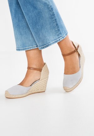 Světlé šedé semišové wedges s pletenou juty na podpatku a hnědým kotníkovým páskem. Okrýlená špička a hladký povrch. Ideální pro neformální nošení.
