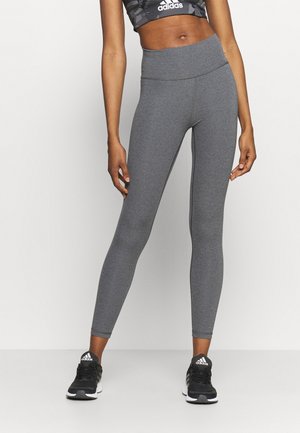 Leggings gris taille haute en tissu stretch, avec une texture lisse et un design ajusté, associés à des chaussures de sport noires.