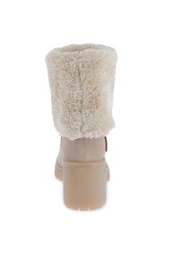 Botín beige hasta el tobillo con un suave y esponjoso cuello de piel. Textura de ante, tacón cuadrado y punta redondeada. Suela de goma con ranuras para mayor tracción.