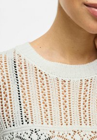 Maglione bianco lavorato a maglia con un design aperto e merlettato, caratterizzato da righe verticali. Collo rotondo e finiture a costine, che enfatizzano la texture.