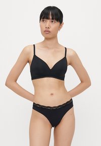 Soutien-gorge noir et string assorti avec une bordure en dentelle festonnée. Tissu doux, bonnets triangulaires et fines bretelles réglables.