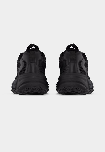 Ζευγάρι μαύρα αθλητικά παπούτσια, εμφανιζόμενα από πίσω πάνω σε λευκό φόντο, με χοντρές σόλες και θηλιές στο τακούνι.