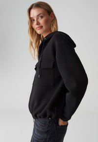 Felpa con zip nera con coulisse, tasca frontale, polsini e orlo a coste. Realizzata in tessuto morbido, con vestibilità comoda.