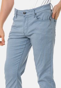 Hellblaue vertikal gestreifte Hose aus weichem Stoff, mit einem klassischen Fünf-Pocket-Design und einem Knopfverschluss am Bund.