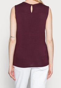 Bordå svart ärmlös topp med design med nyckelhål på baksidan, gjord av mjukt tyg. Har en rundad nederkant och en slät textur.