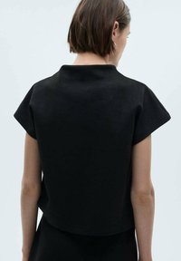 Black, short-sleeve top with a high neckline and a slightly cropped hem. Smooth texture with a minimalist design.
