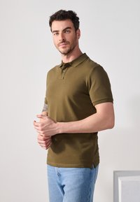 Polo en verde oliva hecho de algodón, con un cuello clásico, mangas cortas y una tapeta de tres botones. Combinado con jeans azul claro.