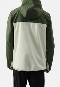 Groene en witte waterdichte jas met capuchon, met een gestructureerde stof aan de bovenkant en een gladde onderkant, elastische manchetten en een trekkoord aan de onderkant.