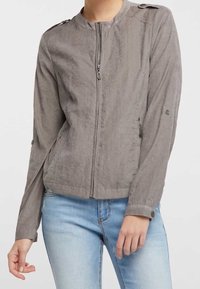 Chaqueta bomber gris con cremallera, cuello redondo, detalles de botones en los hombros y mangas largas con correas ajustables en los puños.