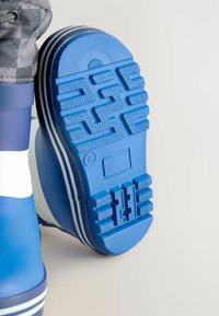 Blaue Gummistiefel mit einer strukturierten blauen Laufsohle, die ein Zickzackmuster aufweist, und drei weißen horizontalen Streifen nahe der Oberkante.