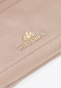 Krémová kožená peněženka s texturovaným povrchem, zlatým logem a akcenty, s viditelným prošíváním podél okrajů.