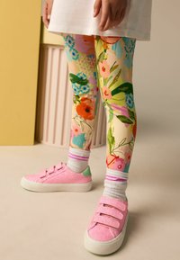 Legginsy w kwiaty mają jasny, mieszany wzór w odcieniach różu, zieleni i niebieskiego. Różowe trampki z brokatem i zapięciami na rzepy.
