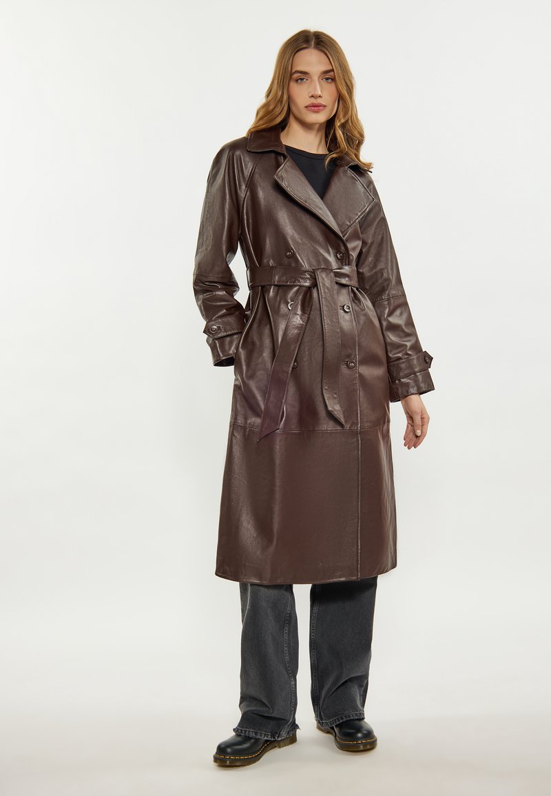 Brun läder trench coat med bälte i midjan, dubbelknäppt framstycke, stor krage och långa ärmar, tillsammans med löst sittande grå jeans och svarta stövlar.