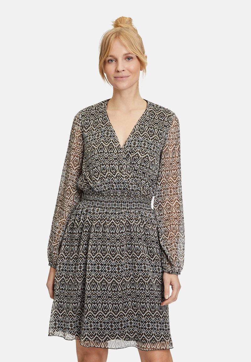 Schwarz-weiß gemustertes Kleid mit V-Ausschnitt, langen transparenten Ärmeln und Gummizug an der Taille, das einen ausgestellten Rock und geometrische Designs aufweist.