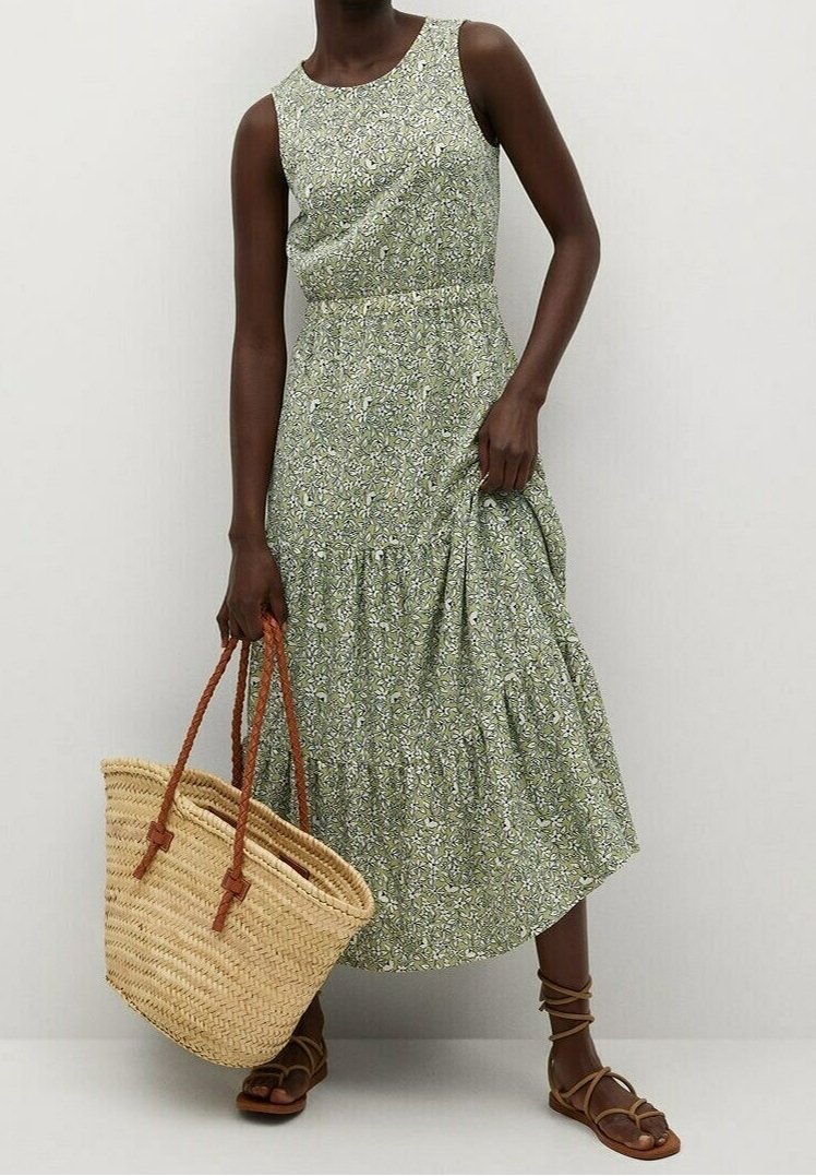 Robe midi florale verte sans manches, avec un ourlet à volants superposés et une taille cintrée. Associée à un sac en paille tressée et des sandales à nouer.