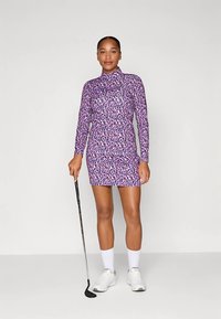 Fioletowa sukienka golfowa z długim rękawem w panterkę, z wysokim kołnierzem i dopasowanym fasonem. W zestawie białe buty sportowe i skarpetki.