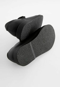 Chaussures noires avec un dessus lisse et une semelle en caoutchouc texturée. Présentent un bout rond et un design minimaliste avec un talon robuste.