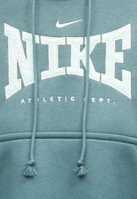 Μπλε-πράσινο φούτερ Nike με μεγάλο λευκό κείμενο "NIKE", μικρό λογότυπο Swoosh από πάνω και κορδόνια που κρέμονται μπροστά.