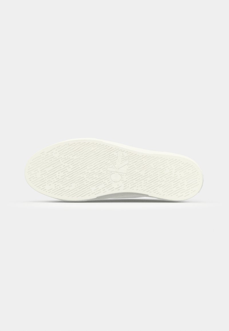 Semelle de sneaker blanche en caoutchouc texturé, avec un logo circulaire et des lignes directionnelles pour une meilleure traction. Design minimaliste, finition lisse.