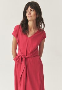 Abito rosso con maniche corte, scollo a V e dettaglio con vita stretta. Tessuto liscio e design fluido. Silhouette semplice, priva di decorazioni e di motivi.