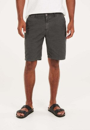 Shorts grigi in cotone con una vestibilità rilassata, tasche frontali e chiusura con bottone, abbinati a sandali neri con tomaia ampia e suola testurizzata.