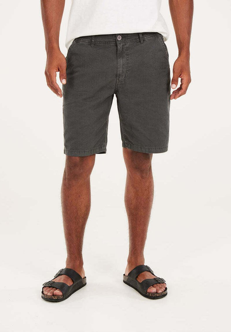 Shorts en coton gris avec une coupe décontractée, poches avant et fermeture à bouton, associés à des sandales noires à larges lanières et à semelle texturée.