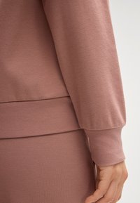 Langzaam sweatshirt met lange mouwen van zacht, roze materiaal, met geribbelde manchetten en een gebande zoom. Heeft een ontspannen pasvorm en een naadloze textuur.