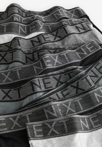 Zwarte, grijze en lichtgrijze boxershorts met elastische banden waarop "NEXT" in een herhalend patroon is gedrukt. Zachte katoenen textuur, verschillende maten.