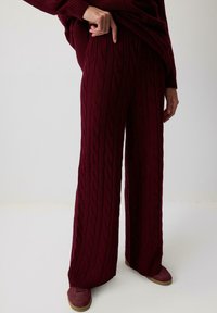 Burgundi värvi kootud laiad püksid tekstuurse mustriga, kõrge vöökoht ja soonikuga mansettidega. Koos sobivate kingadega.