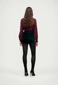 Burgundi pikad varrukad blouse nööbiga mansettidega, mille alla on sobitatud tumerohelised sametist kõrge talje ja täpid kaunistatud lühikesed püksid. Mustad retuusid ja kontsakingad.