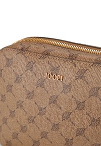 Borsa in tessuto marrone con texture, dotata di una cerniera dorata e del logo "JOOP!", con un motivo dettagliato a ripetizione impresso sulla superficie.