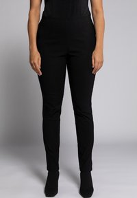 Pantaloni neri intrecciati con vestibilità slim, caratterizzati da una texture liscia e una vita di medio rialzo, abbinati a stivaletti neri a punta.