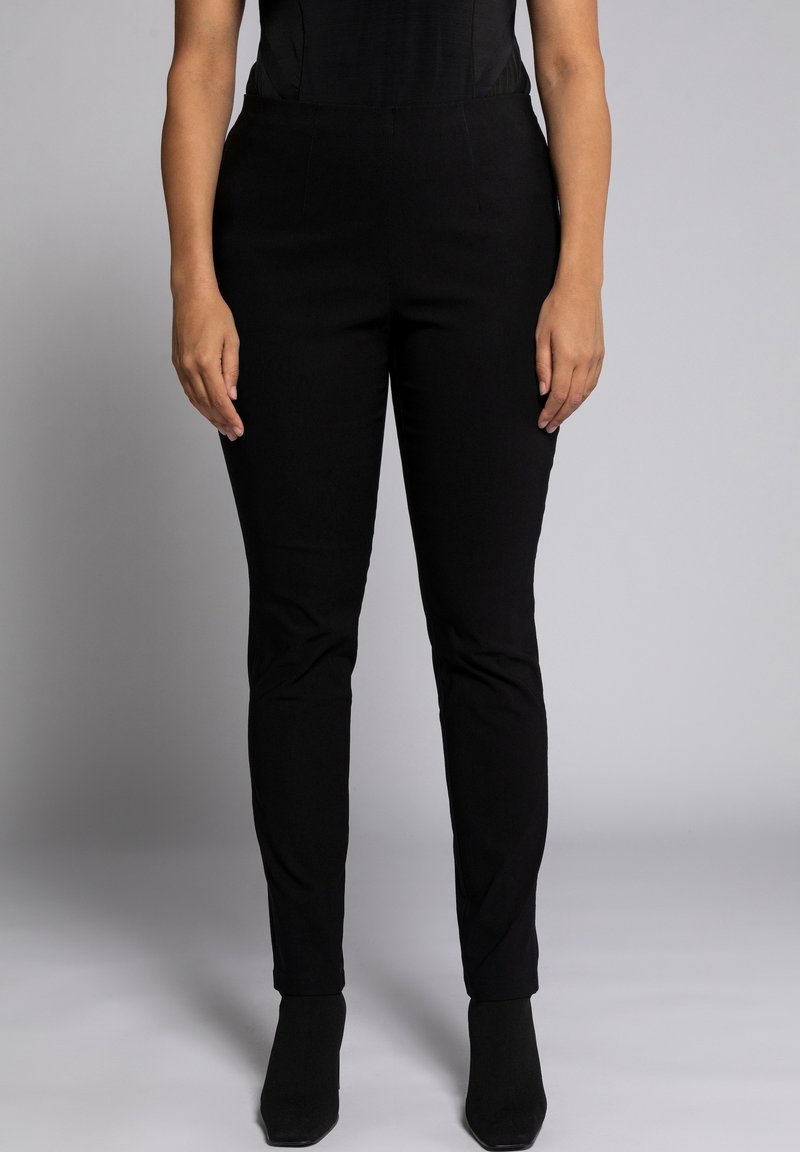 Pantaloni neri intrecciati con vestibilità slim, caratterizzati da una texture liscia e una vita di medio rialzo, abbinati a stivaletti neri a punta.